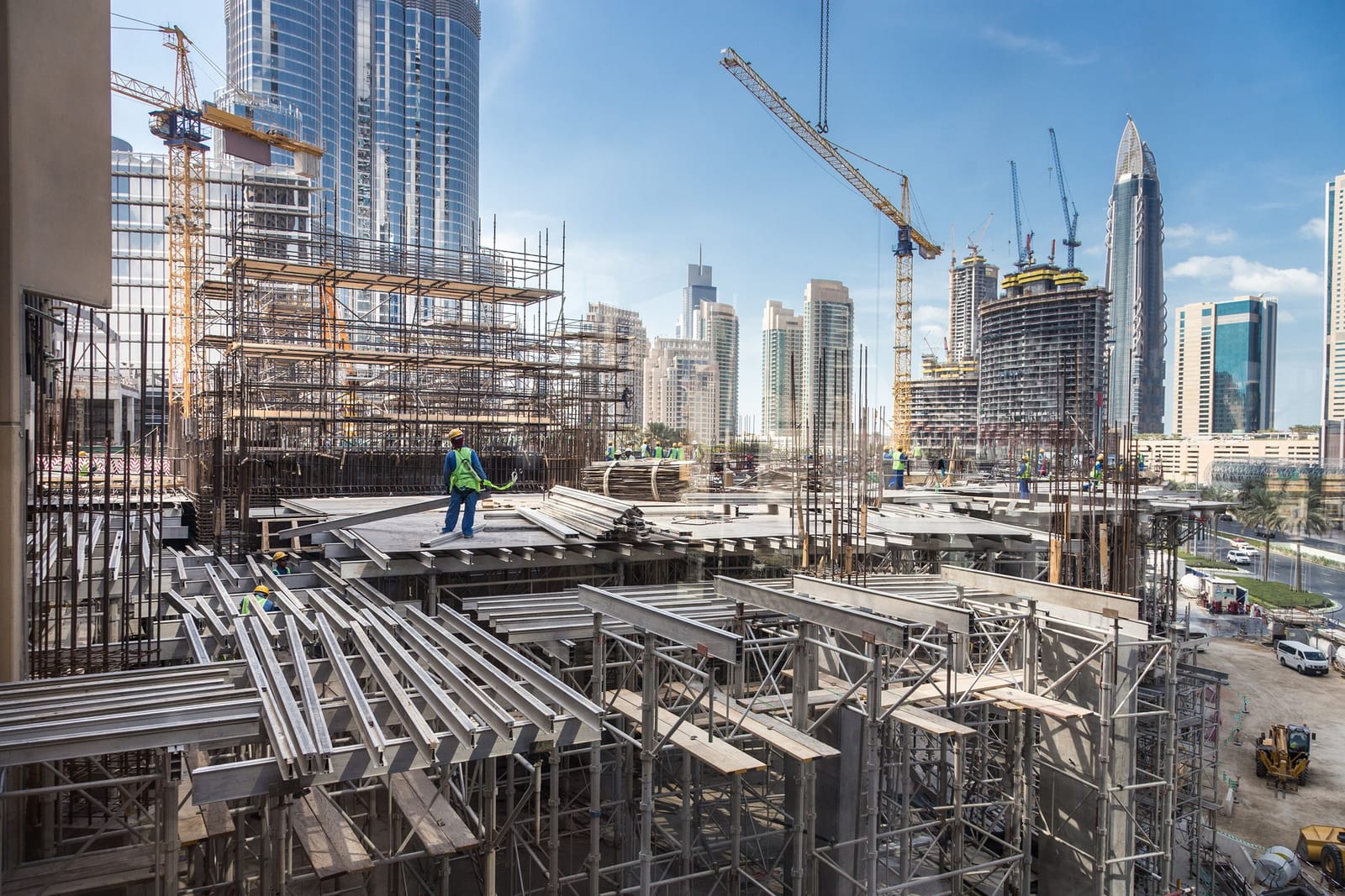Workers on a high-rise concrete frame with a city skyline behind, a developer's asset taking shape