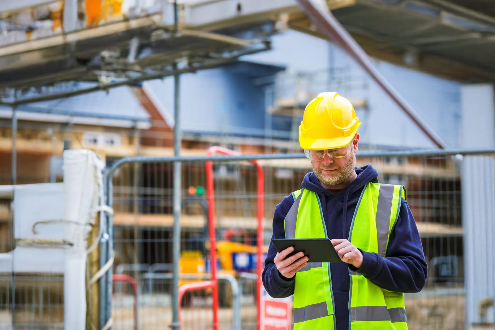 Site inspector in hi-vis recording a fire safety check on a tablet outside a building under construction