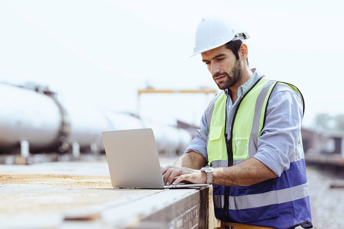 Engineer working on a laptop beside rail tank cars, connecting site data to other systems