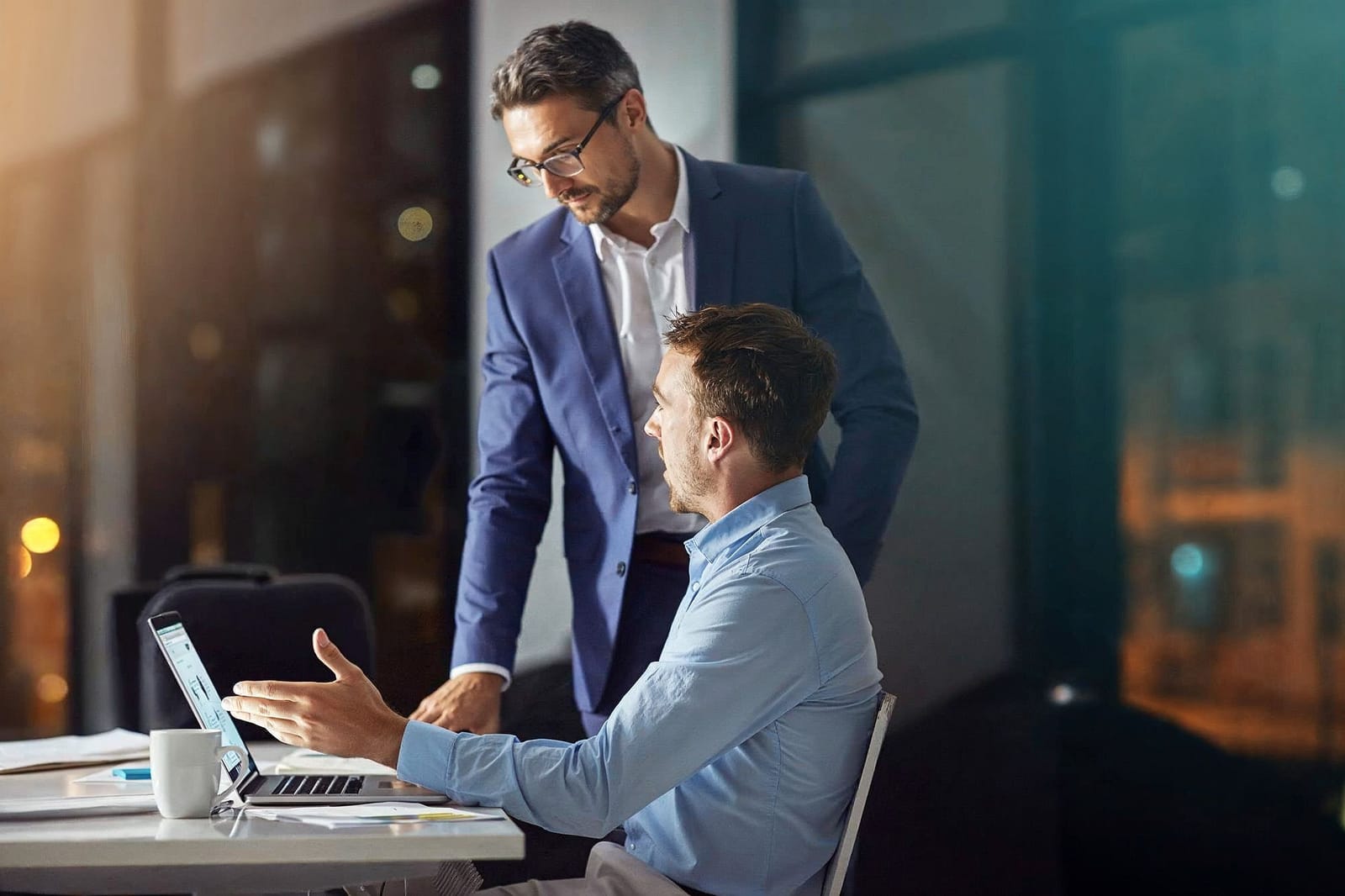 Facilities manager and operator reviewing a management plan together on a laptop in an evening office