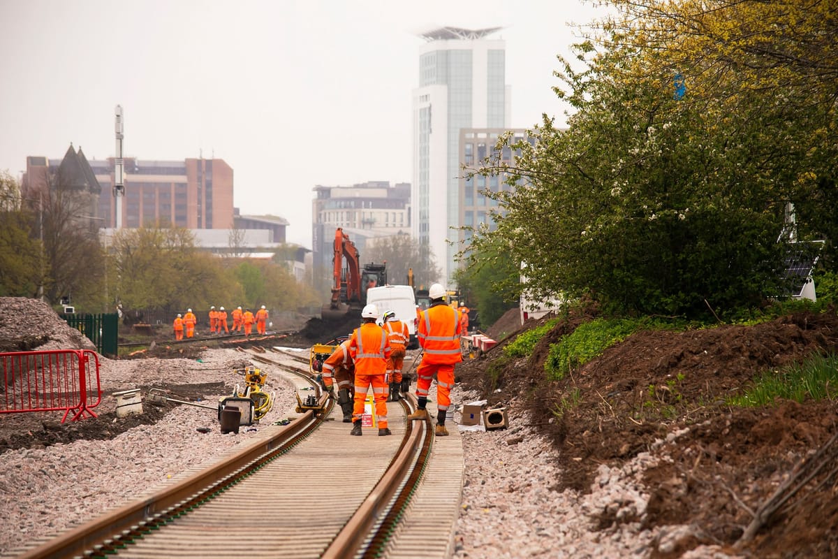 Track workers in orange PPE renewing a railway line beside a city skyline