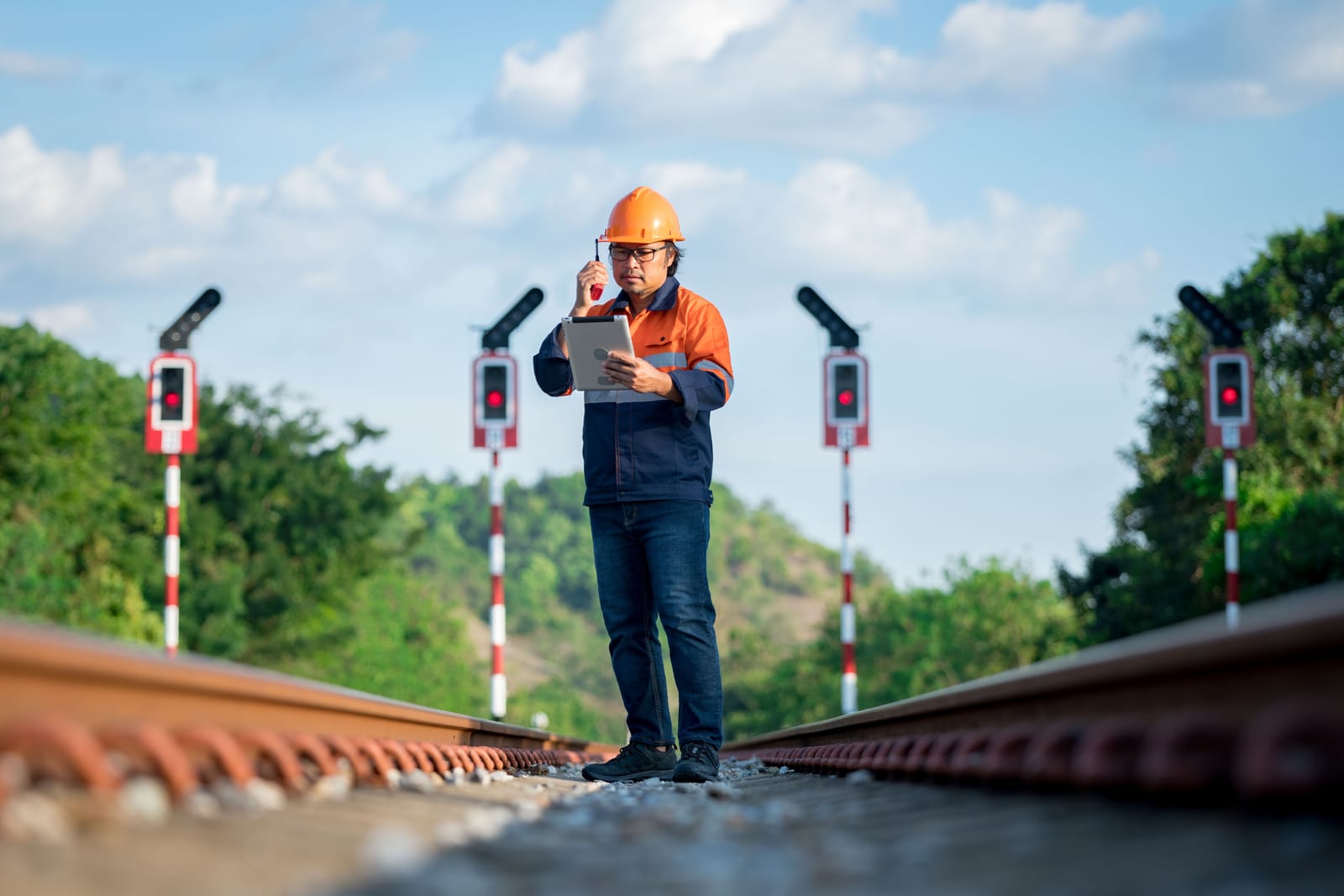 Railway engineer standing on the track with a tablet, inspecting signalling and construction work