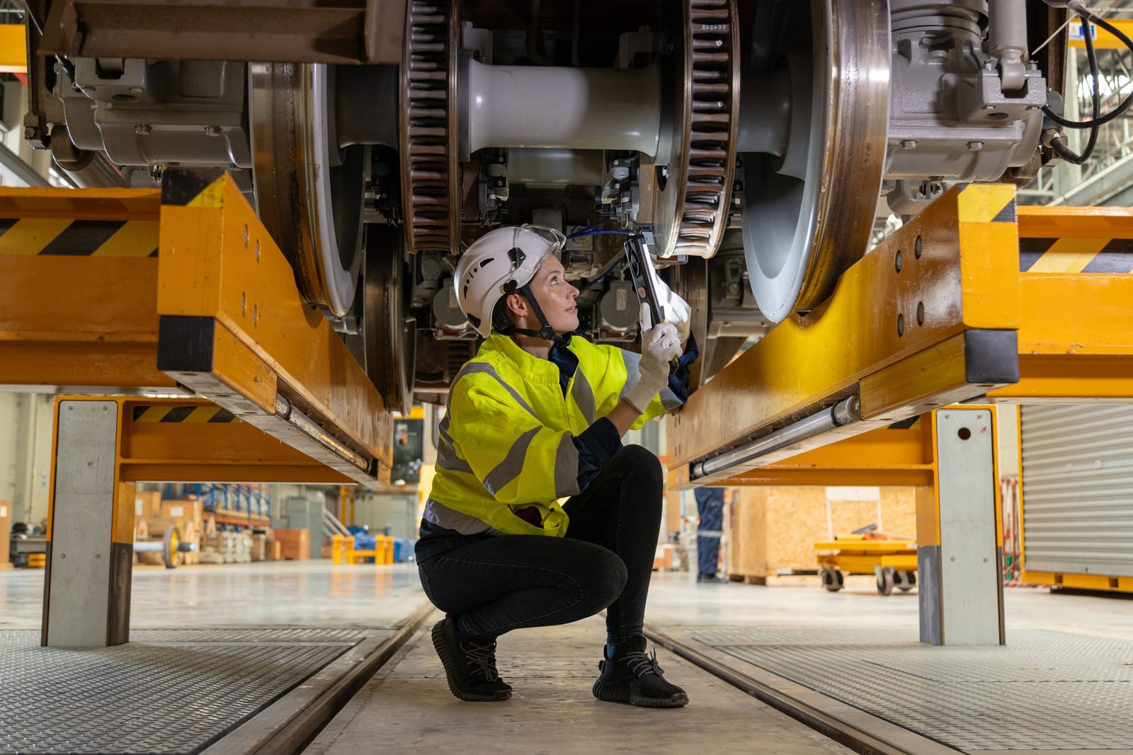 Maintenance technician inspecting a train wheelset from beneath the vehicle in a depot workshop